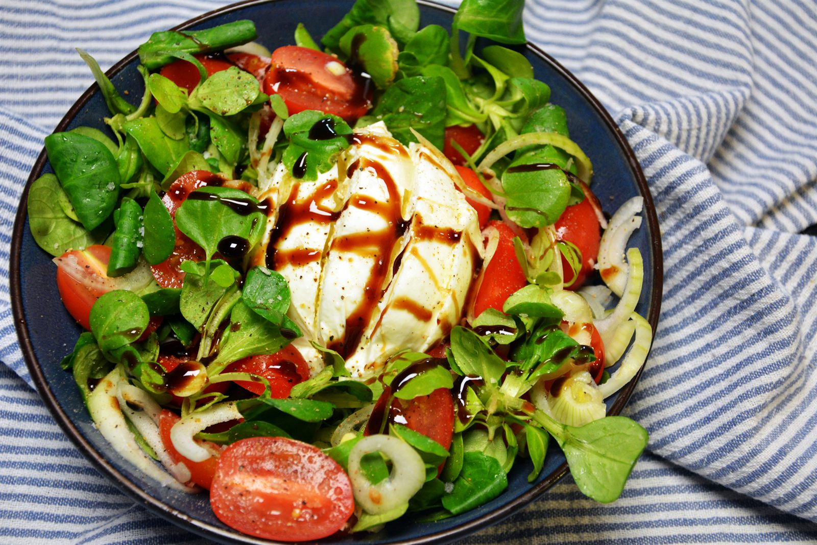 Burratasallad med halverade körsbärstomater i flera färger, babyspenat, rödlök och balsamicoglaze på ett fat