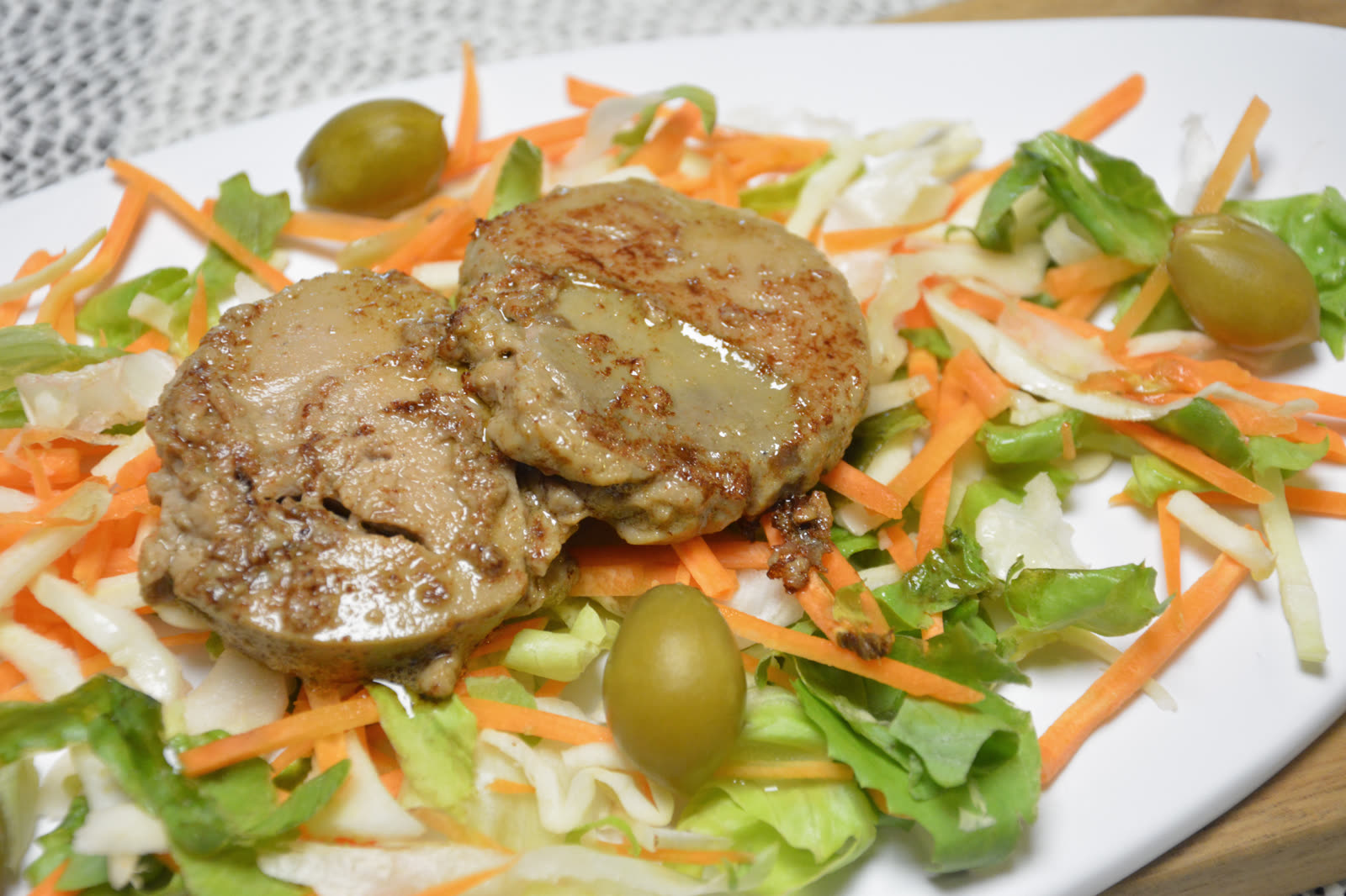 Stekt foie gras i två runda skivor på en bädd av sallad med morot, vitkål och gröna babypersikor