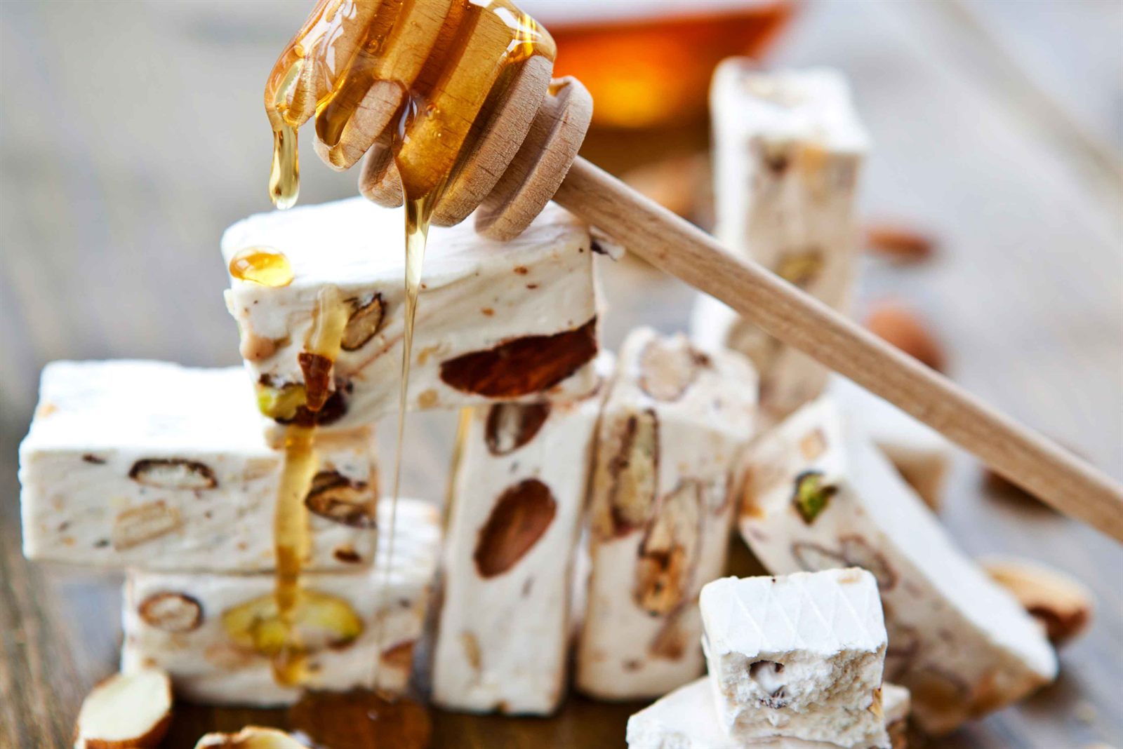 Bitar av vit fransk nougat med hela mandlar och pistagenötter staplade på ett träbord medan honung droppar ner över dem