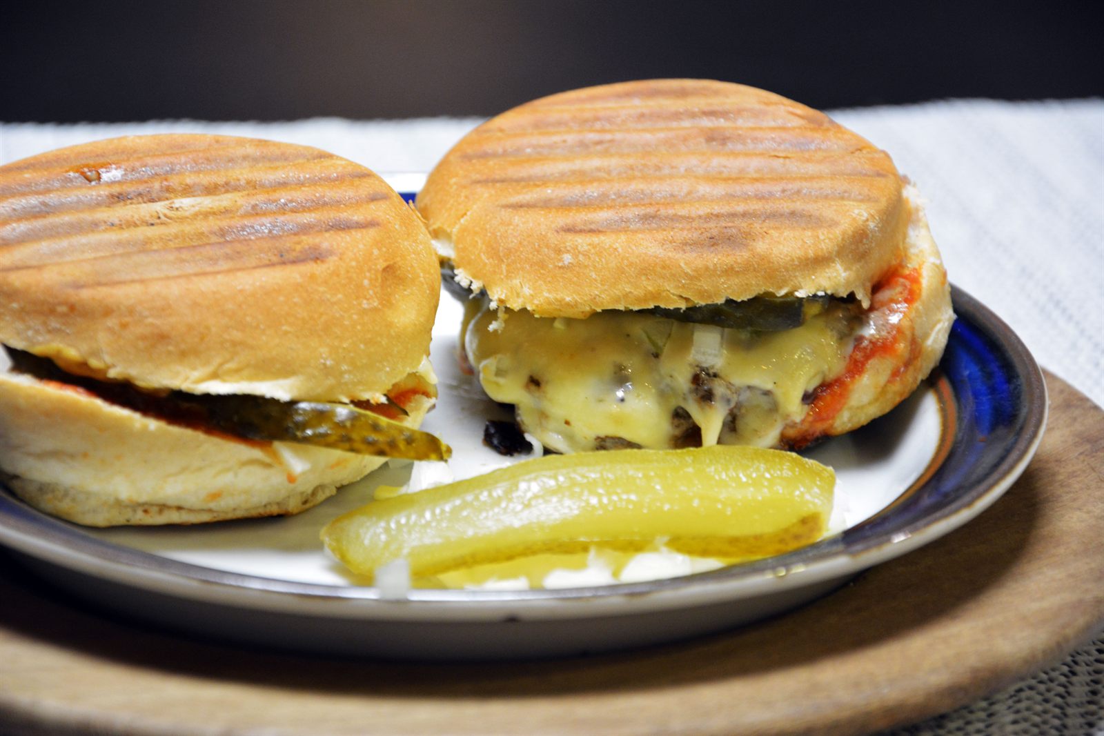 Två hemmagjorda hamburgare med grillränder på brödet, smält ost och inlagd gurka på en tallrik
