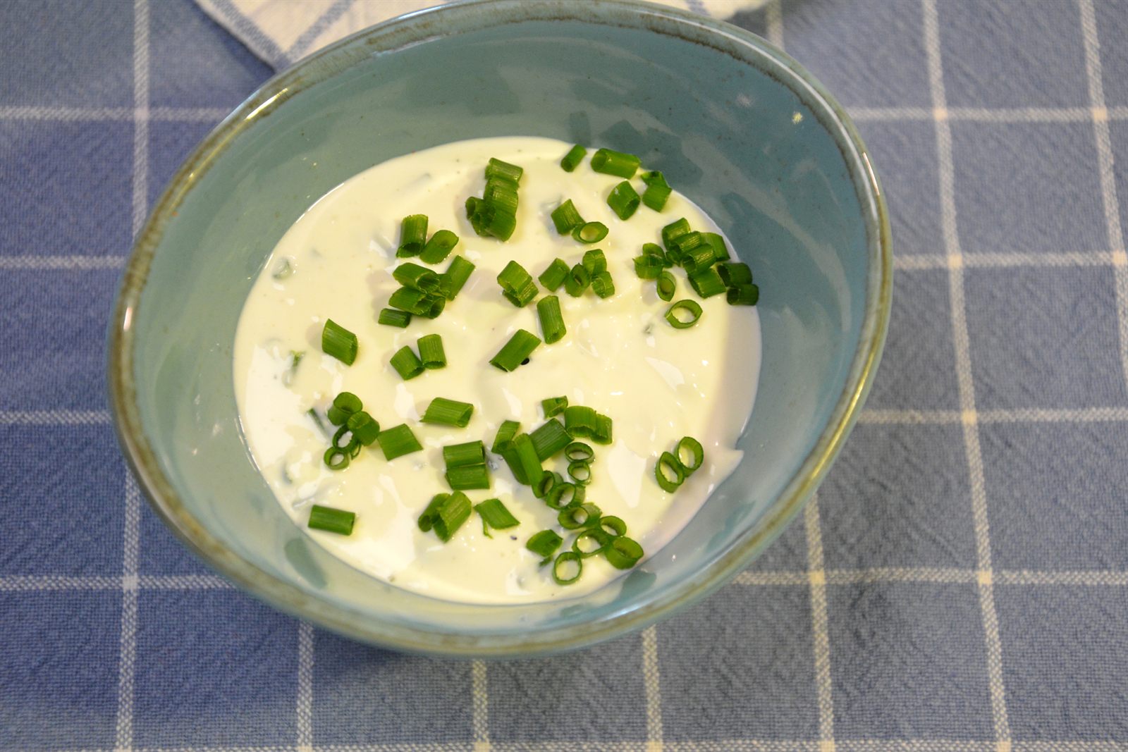 Krämig salladsdressing med gräslök i en turkos skål på en blårutig kökshandduk