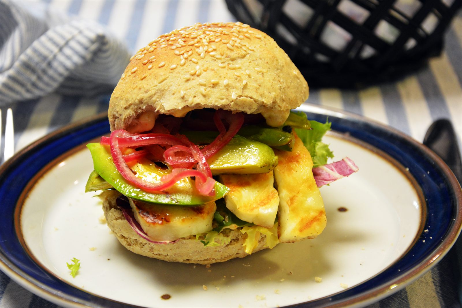 Halloumiburgare i sesambröd med grillstekta halloumiskivor, avokado, picklad rödlök och sallad på en tallrik
